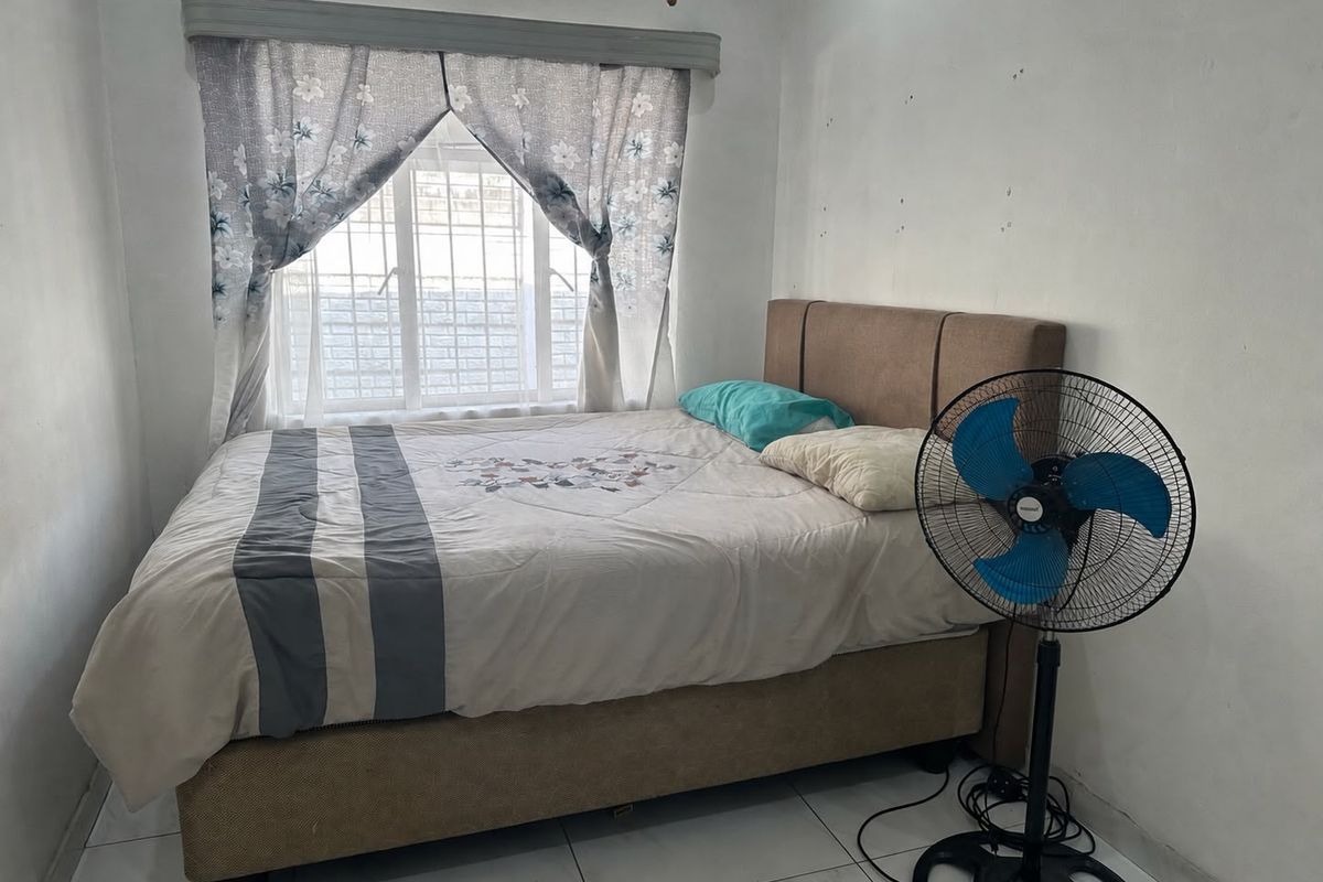 A compact bedroom featuring tiled flooring and a window fitted with security bars, requiring minor wall repairs and cosmetic updates.