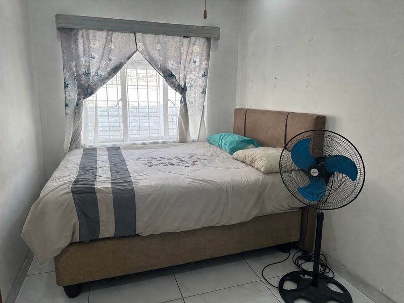 A compact bedroom featuring tiled flooring and a window fitted with security bars, requiring minor wall repairs and cosmetic updates.