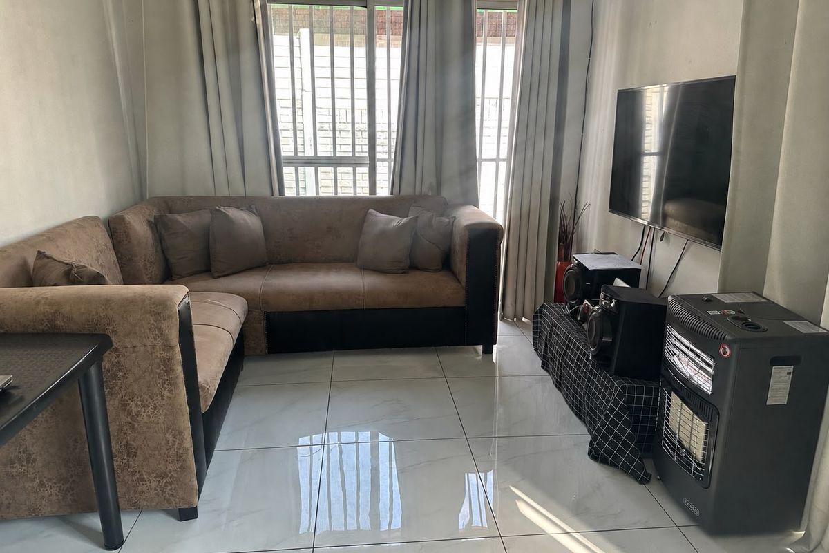 A living room featuring large format floor tiles and natural light through windows fitted with security bars.