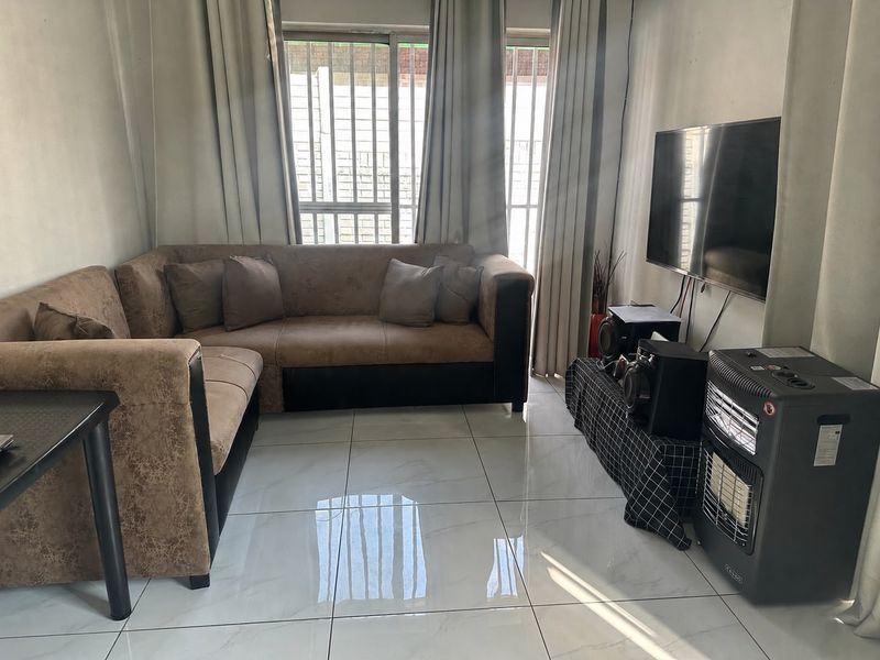 A living room featuring large format floor tiles and natural light through windows fitted with security bars.