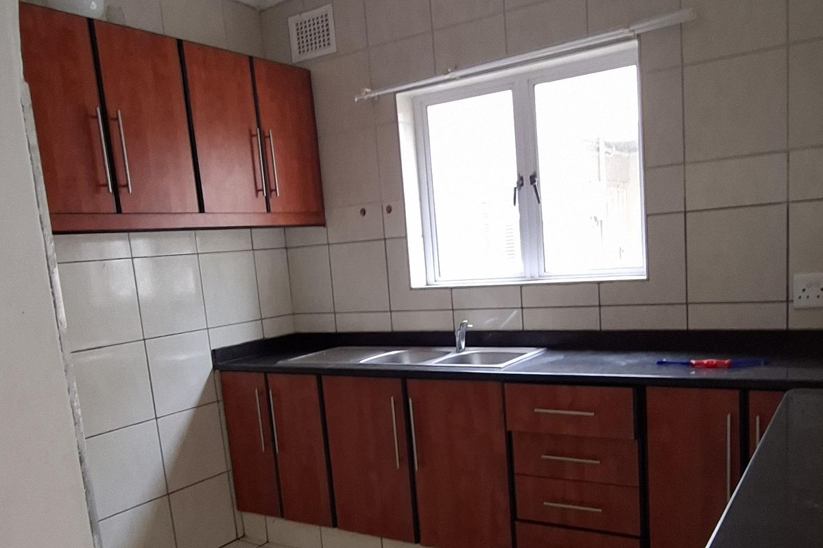 A functional kitchen featuring wooden cabinetry, dark countertops, and tiled finishes. The space requires ceiling repairs due to visible water damage.