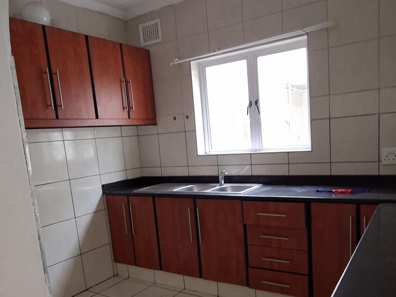 A functional kitchen featuring wooden cabinetry, dark countertops, and tiled finishes. The space requires ceiling repairs due to visible water damage.