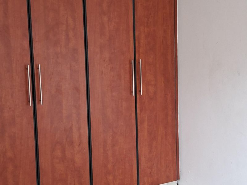A bedroom interior featuring floor-to-ceiling built-in wooden cupboards and neutral tiled flooring.