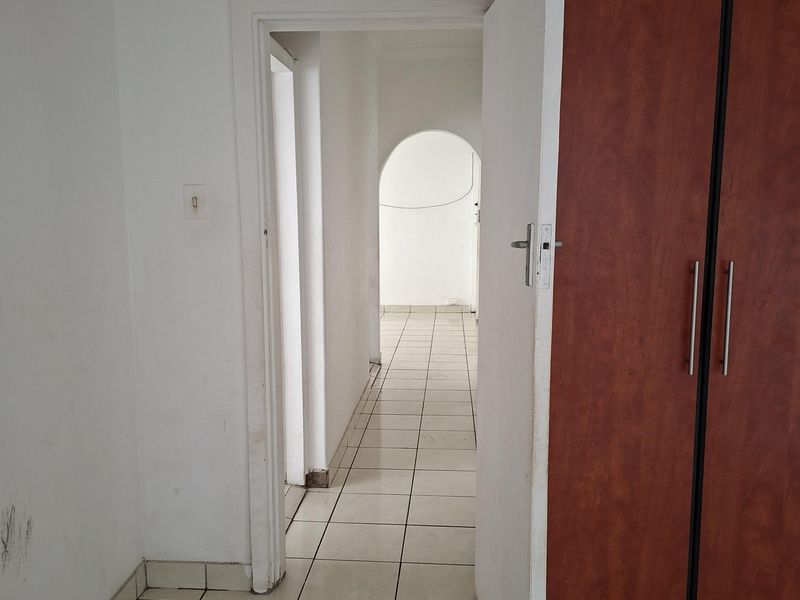 A vacant hallway featuring tiled flooring, built-in wooden cupboards, and an arched transition leading to an adjacent room.