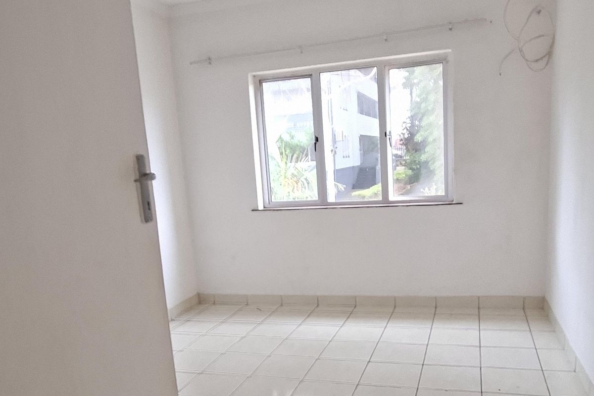 An empty bedroom featuring tiled flooring, an aluminium window, and a curtain rail, requiring minor cosmetic updates and electrical finishing.