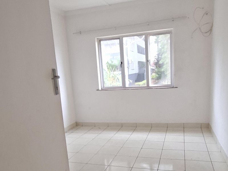 An empty bedroom featuring tiled flooring, an aluminium window, and a curtain rail, requiring minor cosmetic updates and electrical finishing.