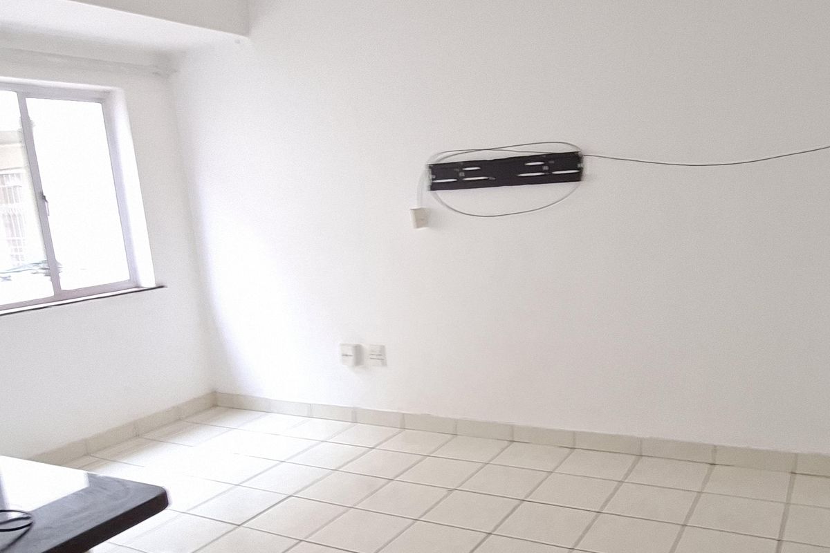 An empty living room featuring white walls, tiled flooring, and a ceiling fan, with a wall-mounted television bracket installed.