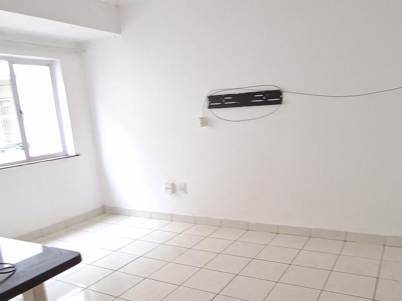 An empty living room featuring white walls, tiled flooring, and a ceiling fan, with a wall-mounted television bracket installed.
