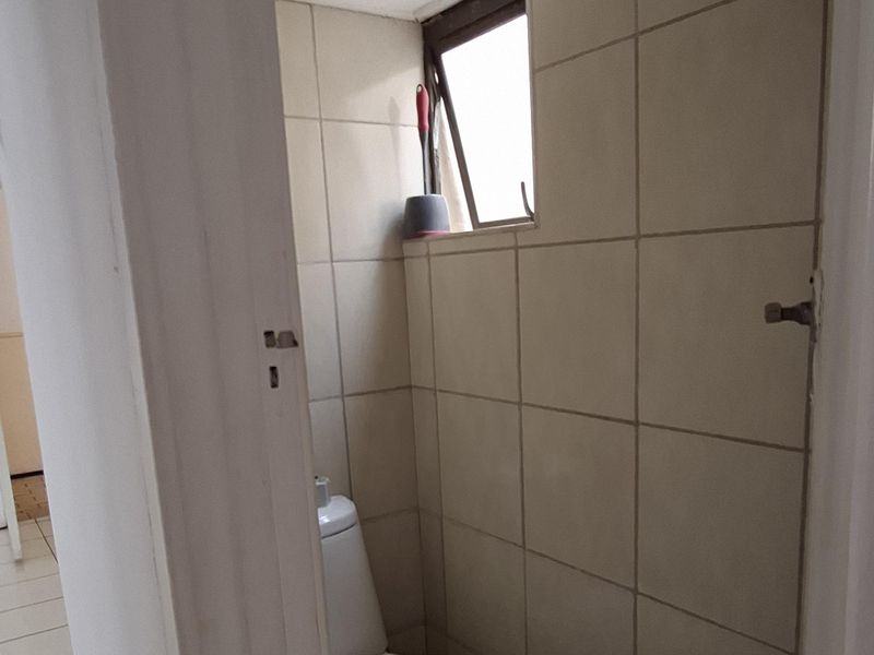 A compact, functional bathroom featuring tiled walls and flooring, a toilet, and a small top-hung window for ventilation.