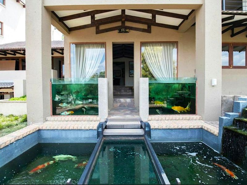 A unique covered patio featuring a central walkway bridge flanked by integrated glass-walled koi ponds and exposed timber ceiling beams.