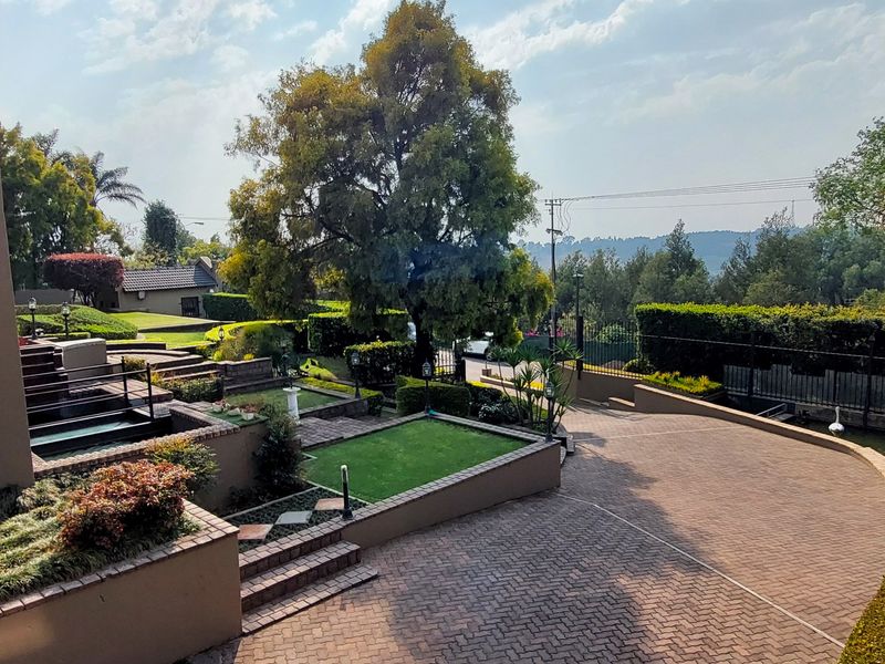 A well-maintained front exterior featuring a paved driveway, terraced garden levels with retaining walls, and a modern glass balustrade overlooking the property grounds.