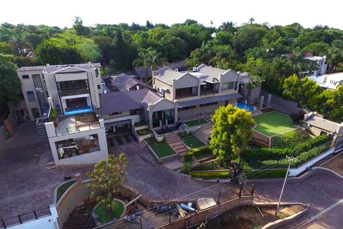 Aerial view of a large multi-level residential property featuring extensive paved areas, a swimming pool, landscaped gardens, and multiple balconies.