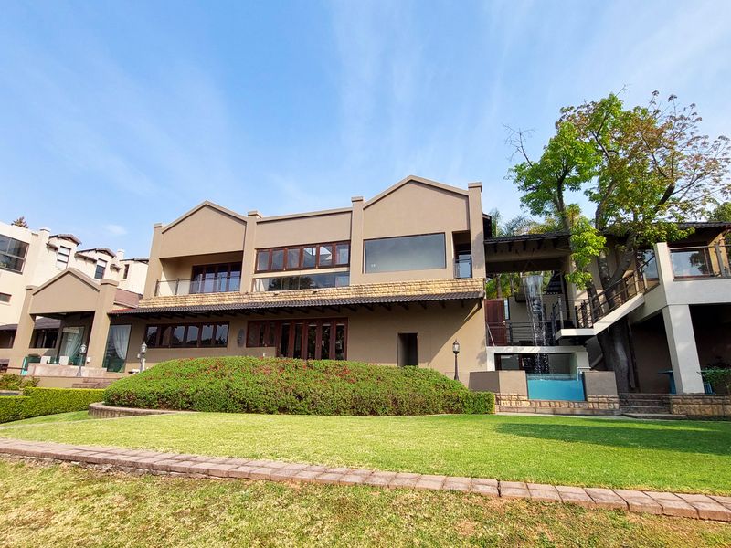 Rear view of a multi-story residence featuring a landscaped garden, swimming pool, water feature, and upper-level balconies with stone architectural accents.
