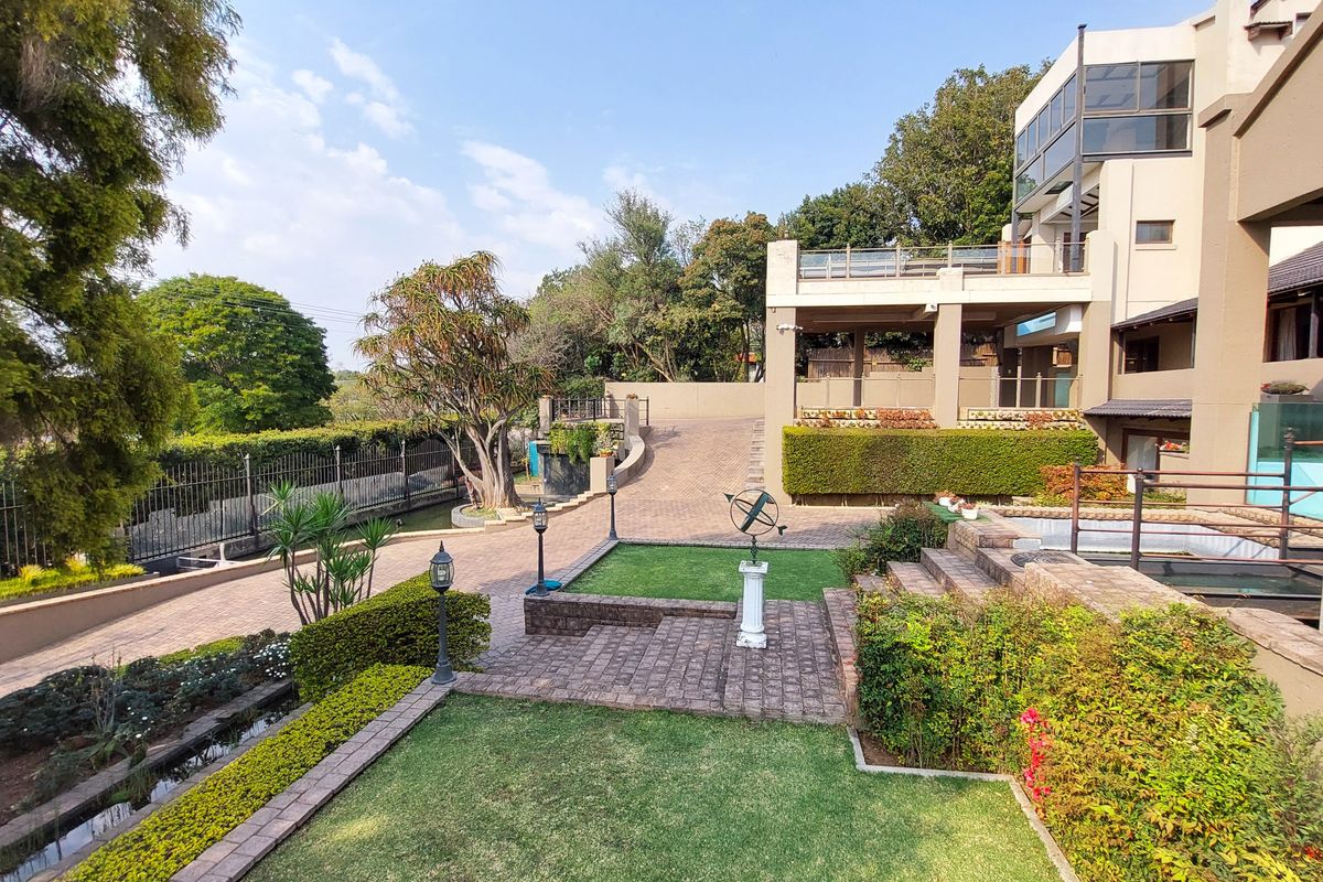 Spacious rear exterior featuring a multi-level landscaped garden, paved driveway, stone terracing, and a large balcony overlooking the property grounds.