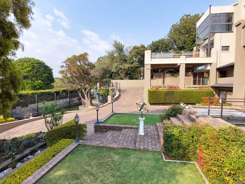 Spacious rear exterior featuring a multi-level landscaped garden, paved driveway, stone terracing, and a large balcony overlooking the property grounds.