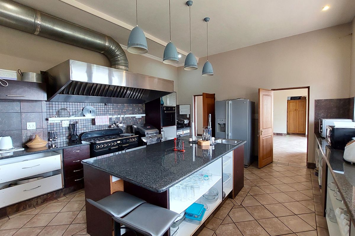 Spacious kitchen featuring a large granite-topped island, stainless steel extractor hood, gas stove, and tiled flooring, offering ample workspace and storage potential.