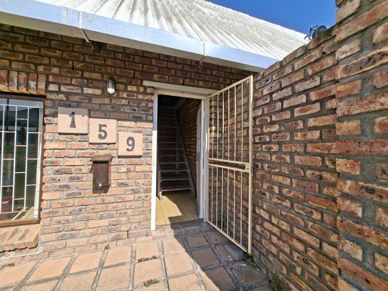 Front entrance featuring a face brick facade, security gate, and external staircase leading to the upper level.