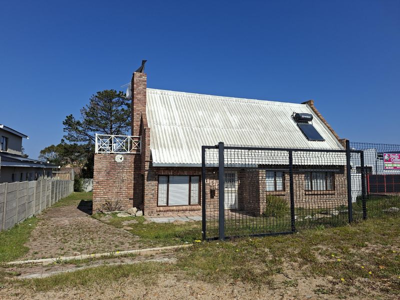 Front view of a face brick house featuring a corrugated metal roof, solar water heating system, and a fenced yard with a paved driveway.
