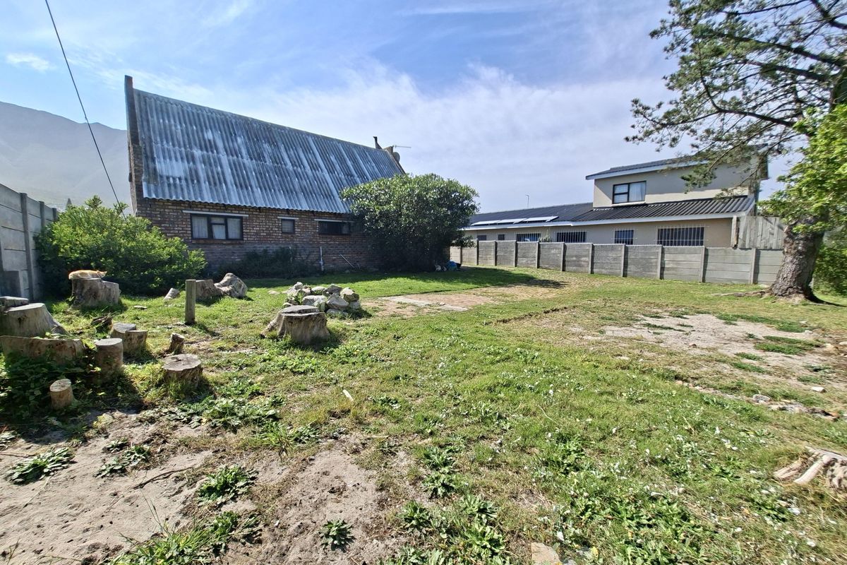 Rear view of the property featuring a brick structure with a corrugated roof, set within a large, unmaintained garden area with boundary walling.