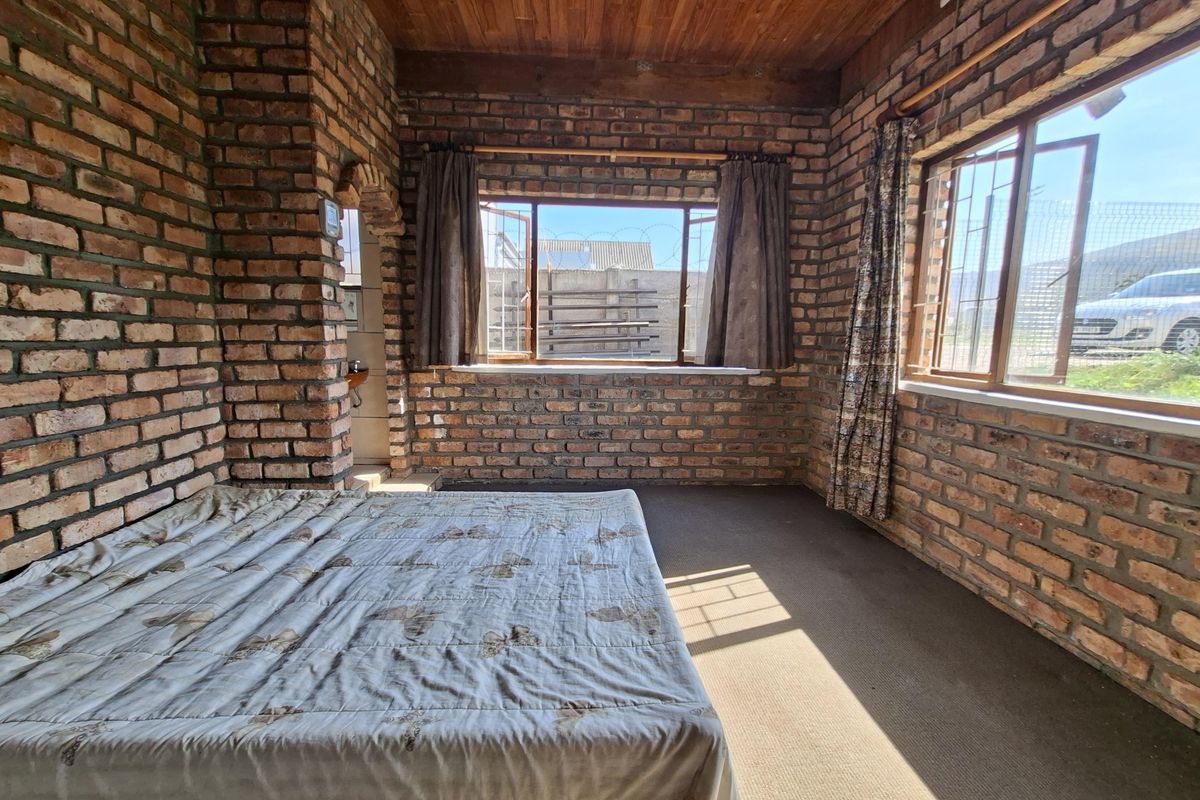 A rustic bedroom featuring exposed brick walls, a timber ceiling, and large windows with security bars, offering a unique industrial-style aesthetic.