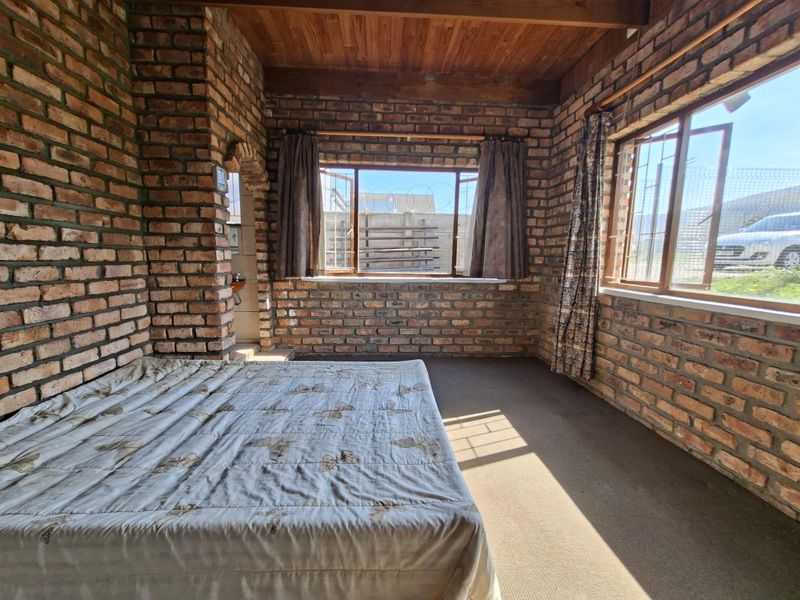 A rustic bedroom featuring exposed brick walls, a timber ceiling, and large windows with security bars, offering a unique industrial-style aesthetic.