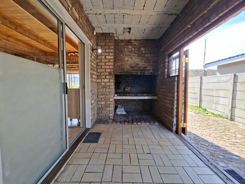 Covered patio area featuring a built-in brick braai, tiled flooring, and direct access to the garden through a sliding glass door.