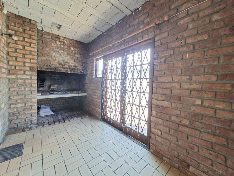 Covered patio area featuring a built-in brick braai, tiled flooring, and sliding door access with security gate.