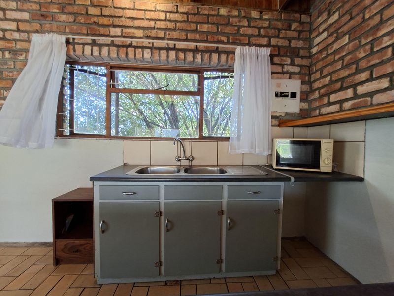 A rustic kitchen area featuring exposed brick walls, a double bowl sink, tiled backsplash, and functional built-in cabinetry.