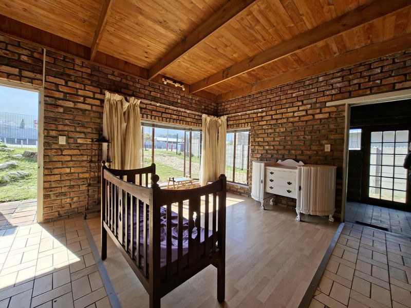Living area featuring rustic exposed brick walls, timber beam ceiling, and a combination of laminate and tiled flooring with access to the garden.