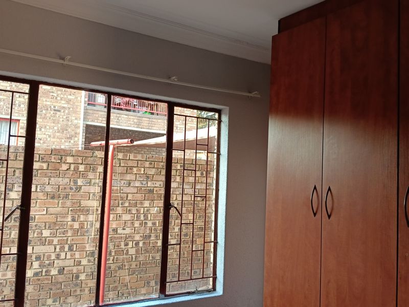 A bedroom featuring a built-in wooden wardrobe and large windows fitted with security bars, offering a view of the exterior brick wall.