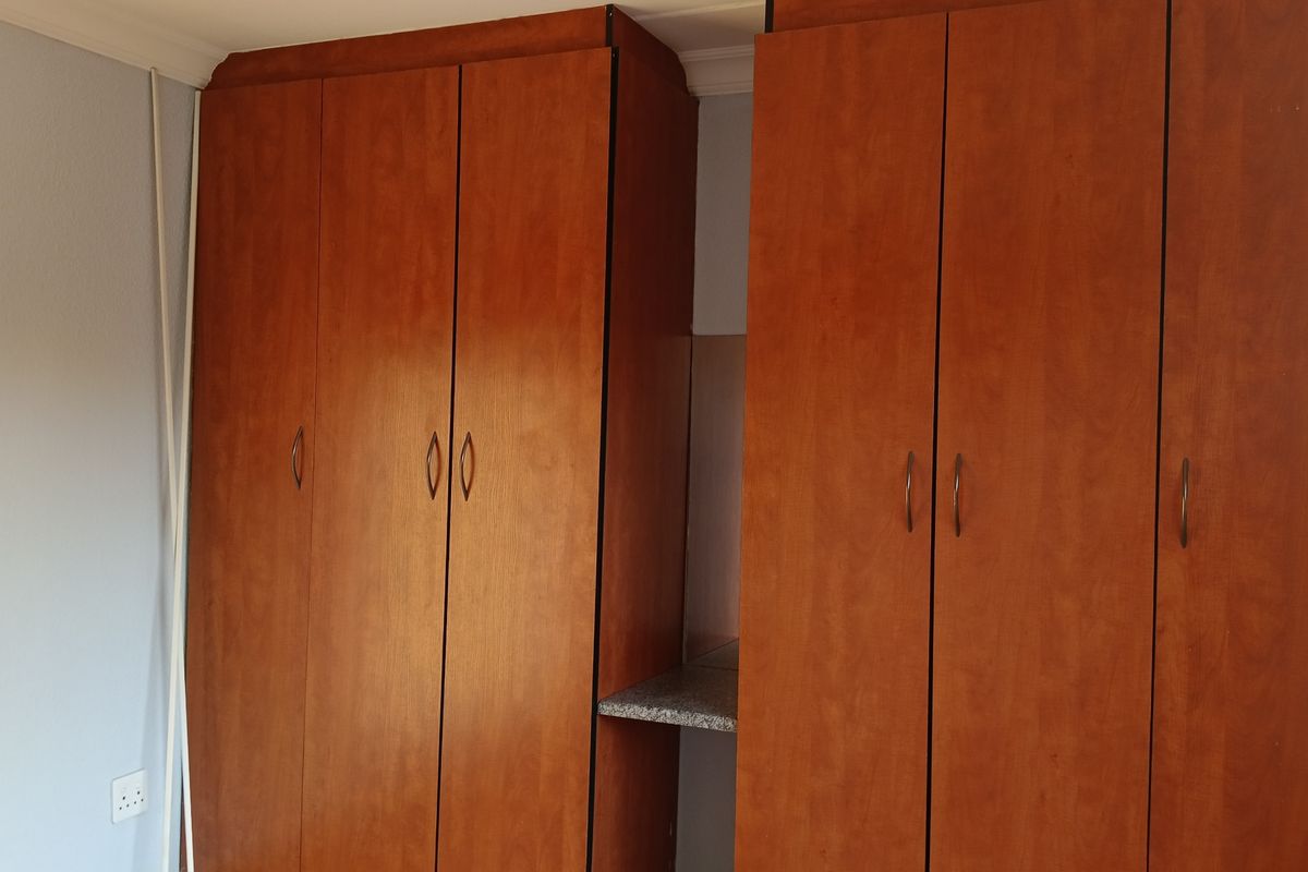 A bedroom featuring floor-to-ceiling wooden built-in cupboards with ample storage space.