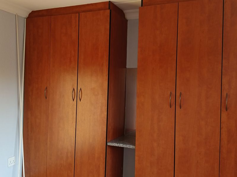 A bedroom featuring floor-to-ceiling wooden built-in cupboards with ample storage space.