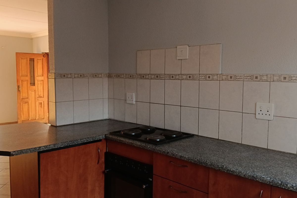 A functional kitchen area featuring built-in cabinetry, a granite-look countertop, an integrated electric hob and oven, and a tiled backsplash.