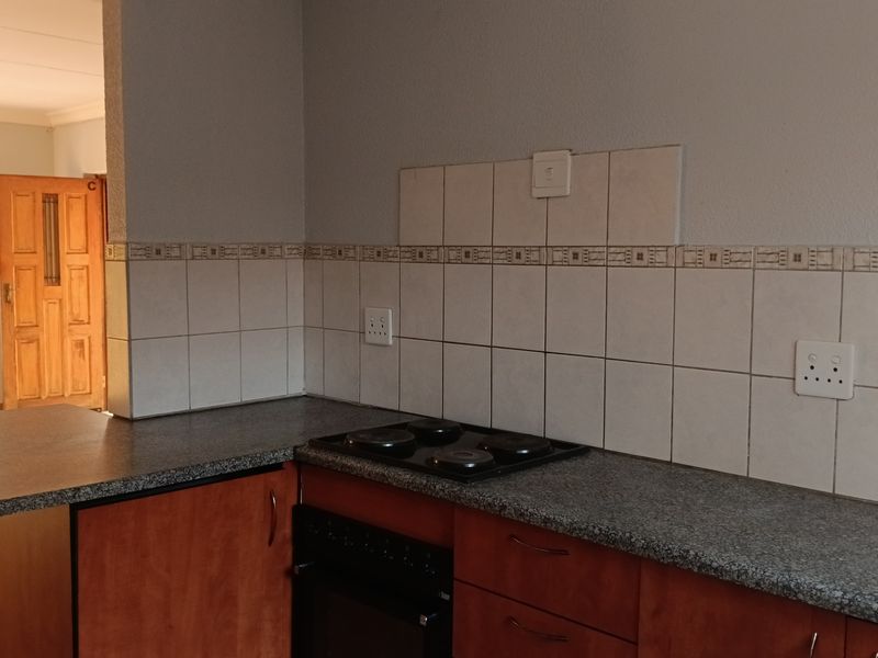 A functional kitchen area featuring built-in cabinetry, a granite-look countertop, an integrated electric hob and oven, and a tiled backsplash.