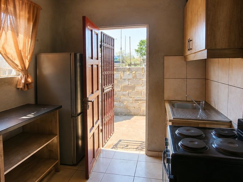 Compact kitchen featuring basic cabinetry, a stainless steel sink, tiled backsplash, and an electric stove, with direct access to an outdoor area.