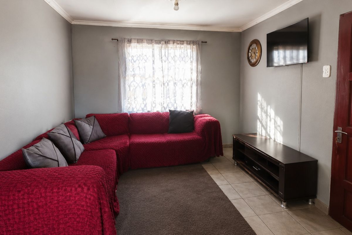 A functional living room featuring tiled flooring, coved ceilings, and a solid timber door, providing a neutral base for interior updates.