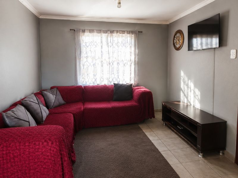 A functional living room featuring tiled flooring, coved ceilings, and a solid timber door, providing a neutral base for interior updates.