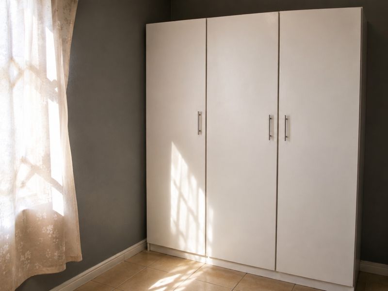 A clean bedroom featuring a large white built-in wardrobe, neutral tiled flooring, and dark grey walls.