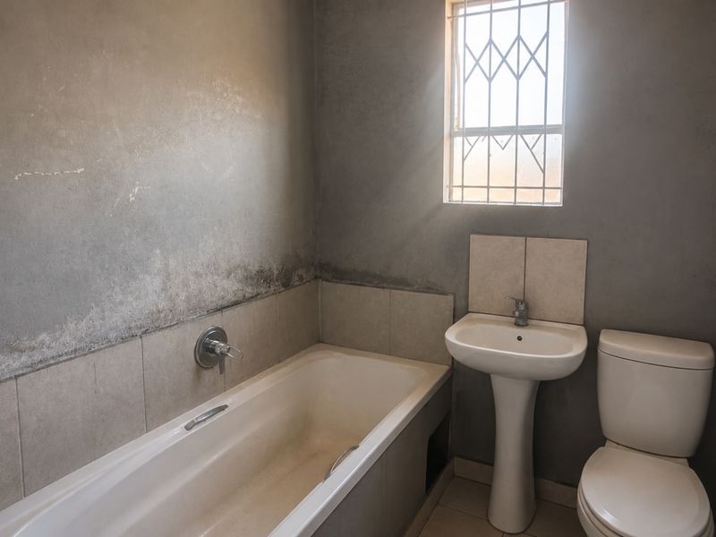 A basic bathroom featuring a bathtub, pedestal basin, and toilet, requiring cosmetic updates and wall finishing to improve its overall condition.