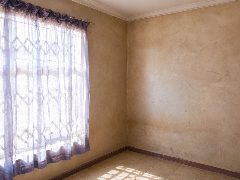 An empty bedroom featuring tiled flooring and a window with a security gate, requiring cosmetic updates to the wall finishes.