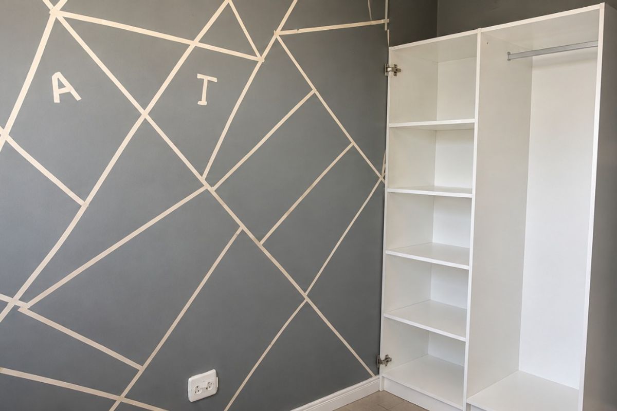 A bedroom featuring a built-in white wardrobe and a decorative geometric wall design, providing functional storage and a modern aesthetic.
