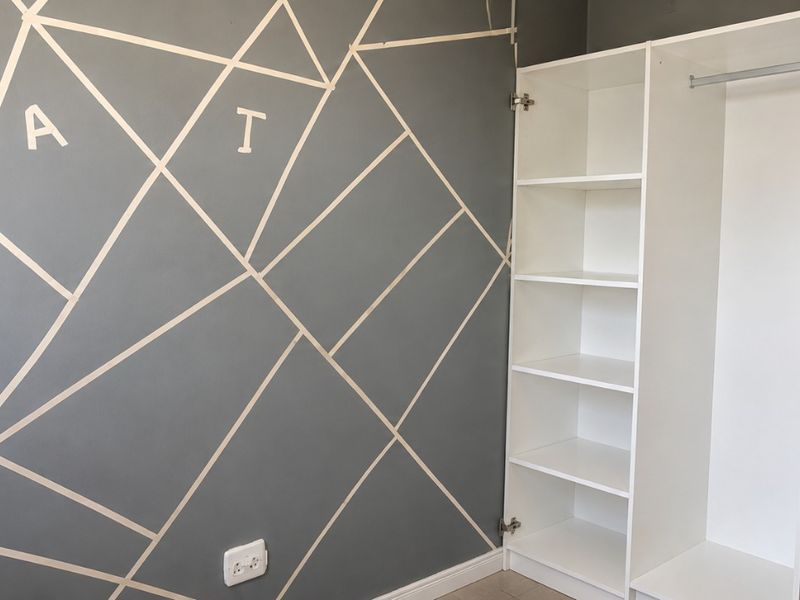 A bedroom featuring a built-in white wardrobe and a decorative geometric wall design, providing functional storage and a modern aesthetic.