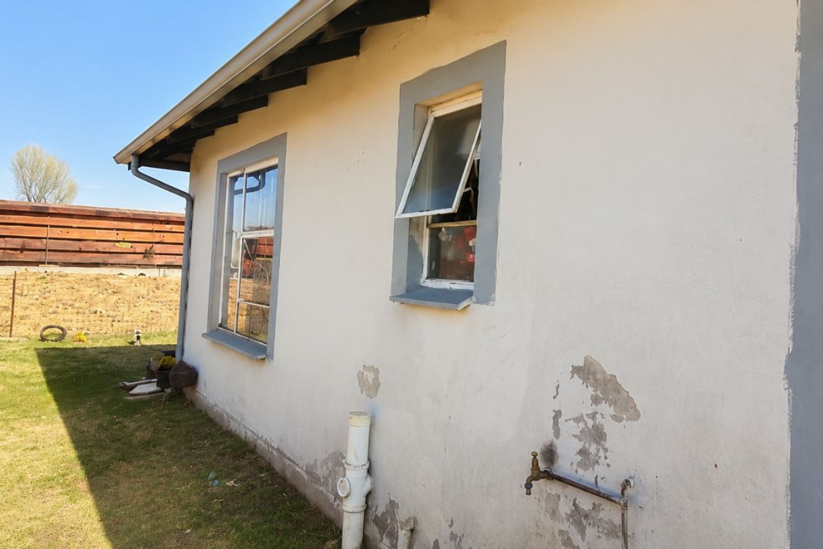 Rear exterior view of the property showing plastered walls with visible paint peeling and plaster damage, external plumbing fixtures, and casement windows.