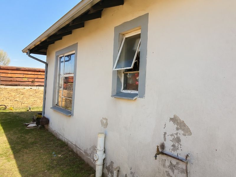 Rear exterior view of the property showing plastered walls with visible paint peeling and plaster damage, external plumbing fixtures, and casement windows.