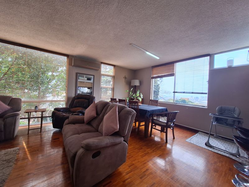 Spacious open-plan living and dining area featuring parquet flooring, large windows with venetian blinds, and an integrated air conditioning unit.