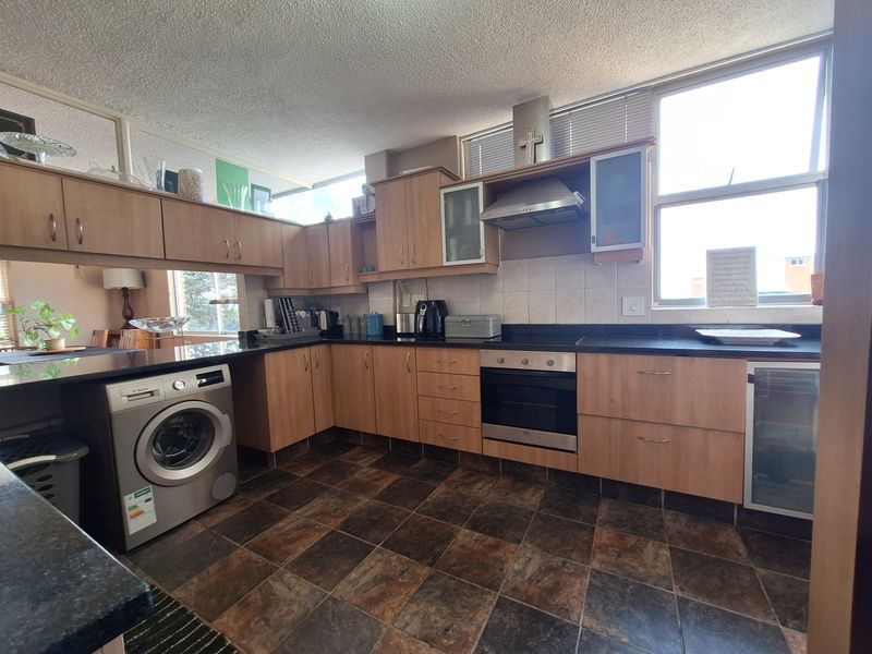 A functional kitchen featuring wood-finish cabinetry, granite countertops, a built-in oven with extractor fan, and tiled flooring with natural light from the window.