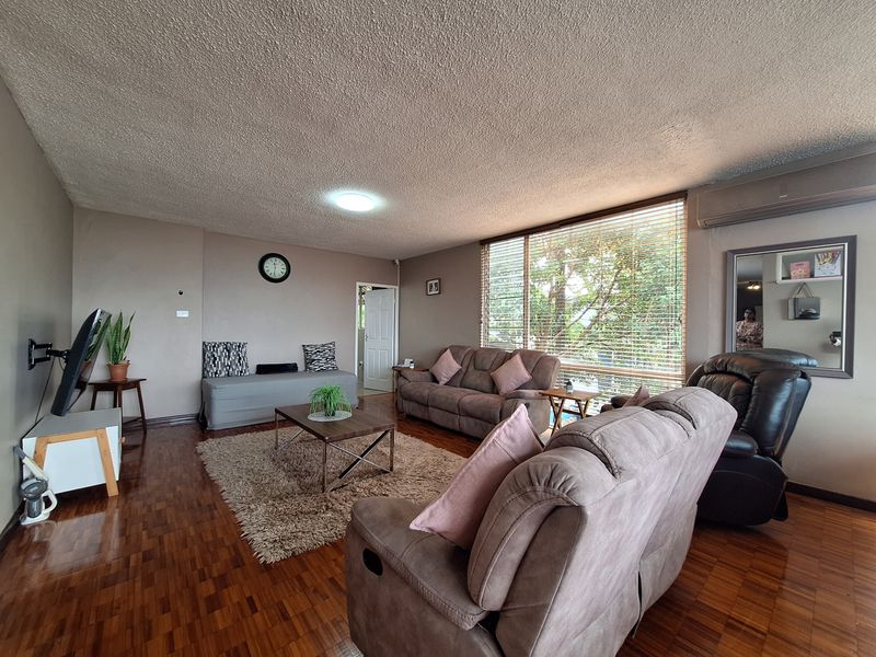 Spacious living room featuring warm parquet flooring, a textured ceiling, and large windows with venetian blinds, providing a comfortable and well-lit living space.