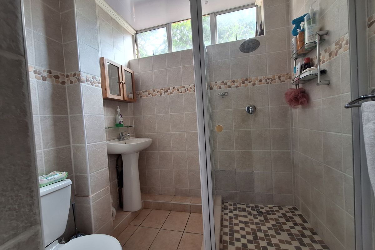 A functional bathroom featuring a pedestal basin, a glass-enclosed shower, and neutral tiled finishes with high-level windows for natural light.