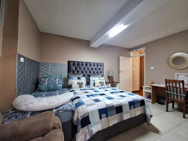 A bedroom featuring tiled flooring, an exposed ceiling beam, and neutral wall tones, providing a functional space with direct access to an adjoining hallway.