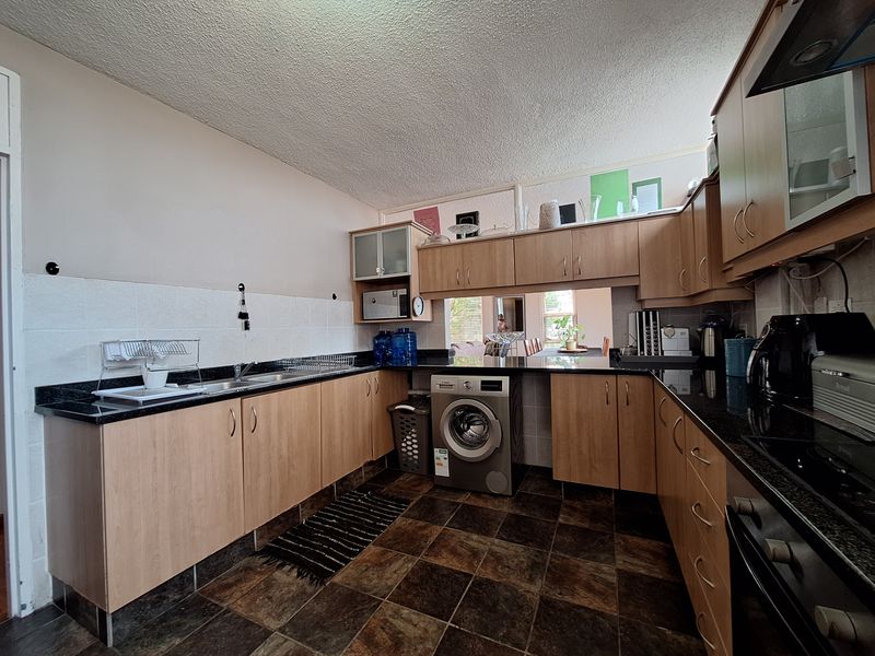 Functional kitchen featuring laminate cabinetry, granite countertops, built-in oven, hob, extractor fan, and integrated washing machine with tiled flooring.